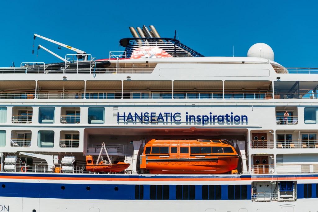 A large white and blue cruise ship, the HANSEATIC Inspiration, in the Nord-Ostsee Canal with an orange ferry in the background